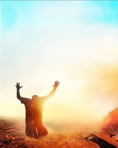 a person kneeling down in the grass with their arms up and hands raised to the sky