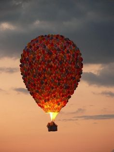 a large hot air balloon flying through the sky at sunset with people in it's back