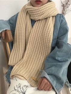 a woman sitting in a chair wearing a knitted scarf over her shoulders and holding a wooden stick