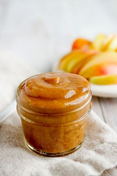 a glass jar filled with peanut butter next to some sliced apples on a white cloth