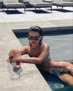 a woman sitting on the edge of a swimming pool with a drink in her hand