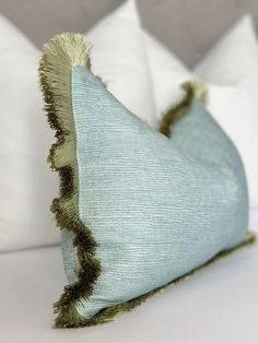 a blue pillow with tassels on it sitting on top of a white bed