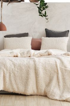 a bed with white blankets and pillows in a room next to a plant on the wall