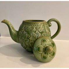 a green teapot with a flower design on the side and a small cup next to it