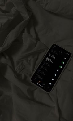 a cell phone laying on top of a bed covered in black sheets and blankets,