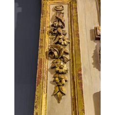 an old wooden frame with gold paint and decorative flowers on it's side, hanging from the wall