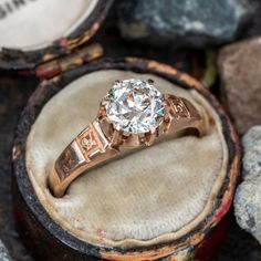 an antique diamond ring sits on top of a wooden box with rocks in the background