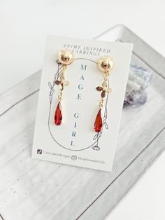 Introducing our Anime Inspired Earring Collection Mage Girl: Gold drop earrings with a fiery red crystal charm, clover connectors, and round 18k gold plated brass ball studs. Cosplay accurate and perfect for everyday wear. Lightweight and 1.5 inches in length. ✧ All earrings are designed by us and made in-house. These earrings were inspired by the characters themselves and are not made to be exact replicas from the game. ✧ These earrings are made with those metal allergies in mind. Earring hooks Earring Collection, Fiery Red, Crystal Charm, Red Crystals, Earring Hooks, Gift For Girlfriend, Anime Inspired, Gold Drop Earrings, Earrings Collection