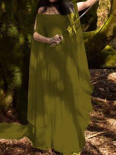 a woman in a green dress standing next to a tree with her hands on her hips