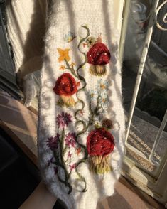 a white sweater with red flowers on it is hanging from a window sill in front of a glass door