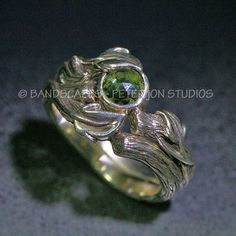 a silver ring with a green stone in the center and leaves on it's sides