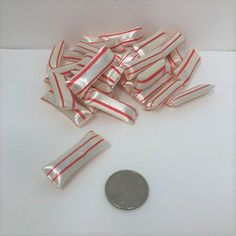 a pile of red and white striped candy wrappers next to a quarter dollar coin