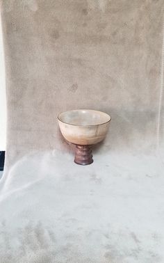 a white bowl sitting on top of a wooden stand in front of a beige wall