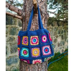 a blue crocheted bag hanging from a tree with a stone wall in the background