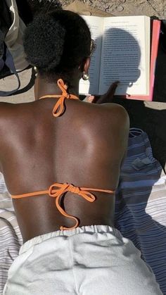 the back of a woman laying on top of a bed with an open book in her lap