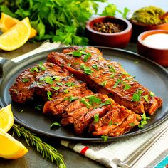 two pieces of meat on a plate with lemons and herbs