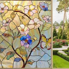 a stained glass window with flowers and butterflies on it in the middle of a garden