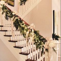 the stairs are decorated with greenery and white ribbon for garlands on each handrail