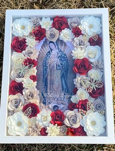 an image of the virgin mary surrounded by red and white flowers in a shadow box