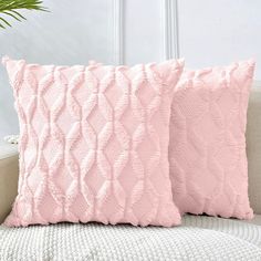 two pink pillows sitting on top of a white couch next to a potted plant