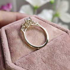 a close up of a gold ring on a pink velvet box with flowers in the background