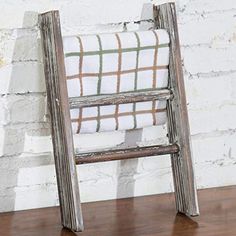 an old wooden ladder leaning against a white brick wall with a plaid blanket on it