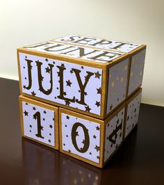 a wooden block with the word july written on it and stars all over it, sitting on a table