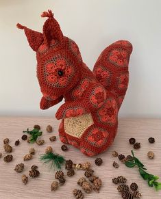 a crocheted squirrel sitting on its hind legs next to pine cones and needles