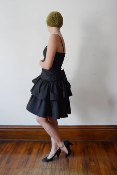 "Description: Black party dress with a drop waist and ruffled skirt. zips up the back and has a large decorative bow. Some tulle under the skirt for fullness. Bodice has boning up the sides. Measurements of garment, allow space for fit. Bust: 32\" some some gathers for cup space. Shown on 36\" and it was way too snug. Waist: 28\" Hips: Open Length: 37\" Skirt length: 15\" I take my measurements flat, and double for circumference. Tag: No brand, just an ILGWU label. Fabric: Polyester Condition: E Party Dress With Ruffle Hem And Fitted Bodice, Flirty Tiered Skirt Evening Dress, Party Dress With Ruffle Hem And Tiered Skirt, Party Mini Dress With Ruffle Hem And Fitted Bodice, Flirty Tiered Skirt Mini Dress For Party, Party Mini Dress With Bow And Fitted Bodice, Voluminous Ruffled Mini Dress For Cocktail, Cocktail Mini Dress With Voluminous Ruffled Skirt, Cocktail Mini Dress With Ruffles And Voluminous Skirt