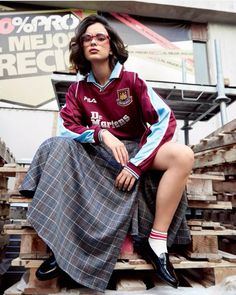 a woman sitting on top of a pile of wooden pallets wearing a skirt and jacket