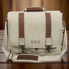 a canvas bag with brown leather straps and the initials b & g on it, sitting on a wooden table