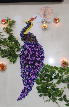 a peacock made out of flowers on the floor next to some candles and greenery