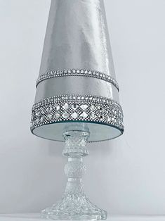 a glass table lamp with a silver shade on it's top and beaded trim around the base