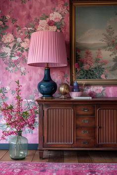 a pink and blue vase sitting on top of a wooden dresser next to a painting