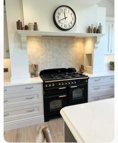 a clock mounted on the wall above an oven in a kitchen with white cabinets and counter tops