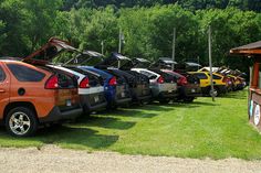 a row of parked cars sitting on top of a lush green field next to a forest