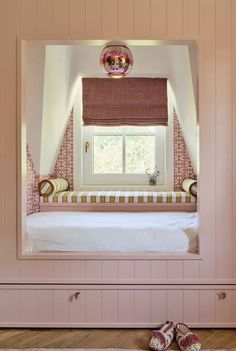 a bedroom with pink walls and white bed in the corner, under a window that has an open curtain