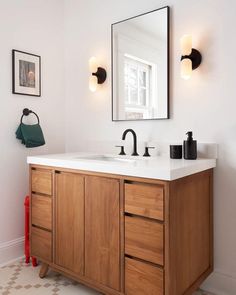 a bathroom vanity with two mirrors and lights on it's sides, in front of a white wall