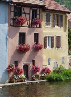 an old building with flowers on the windows and water below it in front of some buildings