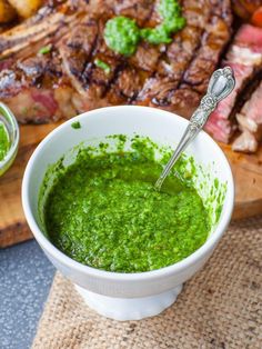 a white bowl filled with green sauce next to meat