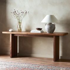 a table with a lamp and vase sitting on top of it next to a rug