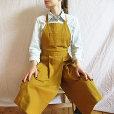 a woman sitting on top of a wooden chair wearing overalls and holding two large bags