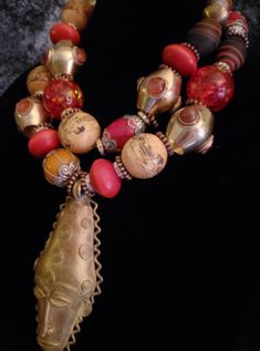 This piece contains numerous high-end, rare and scarce components. The focal point is a lost wax brass African Mask pendant which measures 5" x 2.25". The adjustable double strand necklace measures 18-21" and is finished with gold tone hardware, a lobster claw clasp and a 3" extender chain. The necklace components include Moroccan resin, ornate capped Tibetan resin beads, Tibetan oversized acrylic beads, faux scrimshaw deplicting the Kama Sutra, rhinestone rondelles, metal daisy spacers, inlaid agate vintage brass beads, Nepalese glass, inlaid Tibetan red resin beads, vintage brass beads, Ethiopian copper and a variety of metals. This is really stunning and has what I would describe as a moderate weight. Neither lightweight nor heavy. From the Atelier of Kat Kouture!! Vintage Bronze Beaded Necklaces With Large Beads, Vintage Bronze Beaded Necklace With Large Beads, Artisan Brass Jewelry With Large Beads, Large Bronze Bohemian Beads, Bohemian Large Bronze Beads, Artisan Gold Beads For Festivals, Bohemian Brass Jewelry With Large Beads, Spiritual Brass Jewelry With Large Beads, Festive Bohemian Beaded Necklaces With Gold Beads