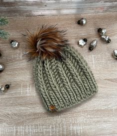 a knitted beanie with a brown pom - pom sits on a wooden surface