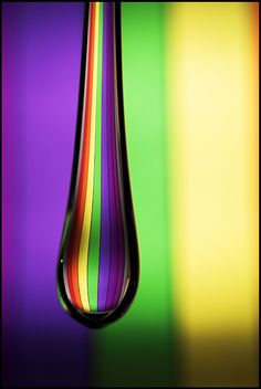 a drop of water that is hanging from a rainbow colored line on the side of a multicolored wall