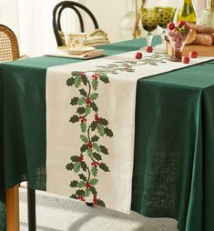 the table is covered with green and white linens, including holly - leaf decorations