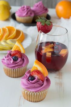 three cupcakes with fruit on top are next to a glass of wine