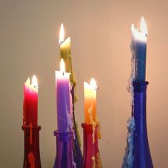 three colorful candles sitting in bottles with water on the bottom and one candle lit up