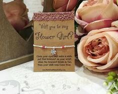 there is a flower girl bracelet on the table next to some flowers and a card that says will you be my flower girl?