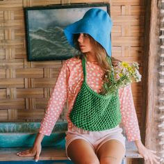 a woman sitting on a bench wearing a blue hat and holding flowers in her hand